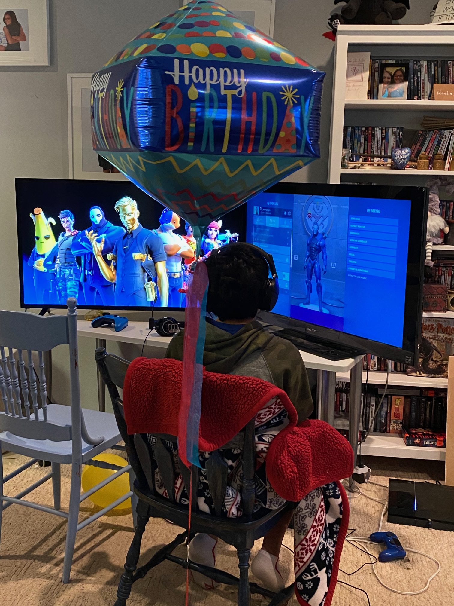 Boy sitting with two televisions and birthday balloon